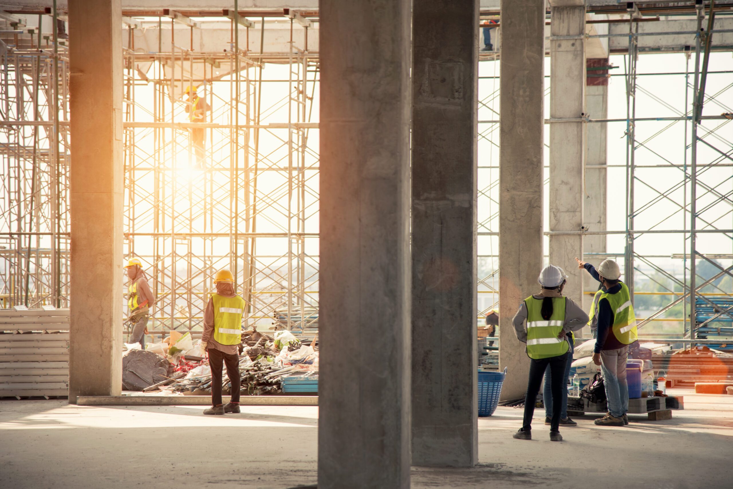 Group of construction workers in safety wear on site with large concrete pillars and scaffolding