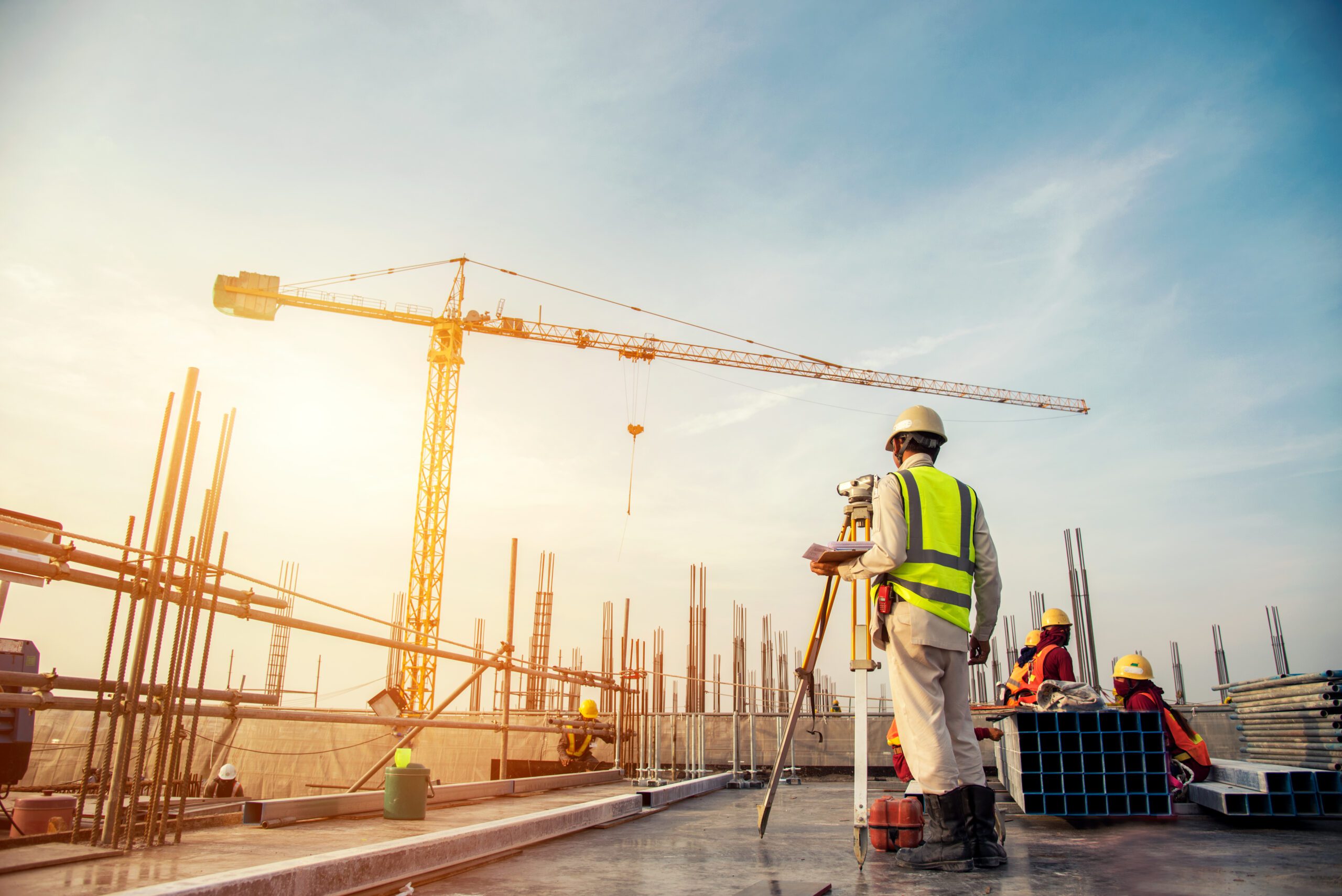 Contractor using survey equipment on construction site with large crane in the background