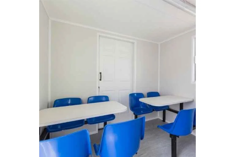 Inside of portable office with white plastic tables and blue chairs