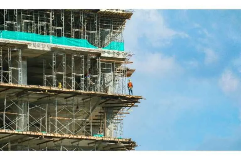 Construction worker on the corner of building that is being constructed, surrounded by scaffolding
