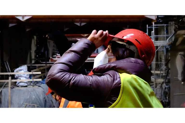 Construction project manager onsite wearing a hi vis vest and red hard hat.