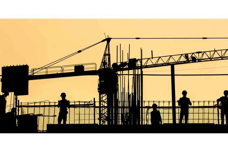 Construction workers photographed working on a building with a crane in the background at sunset