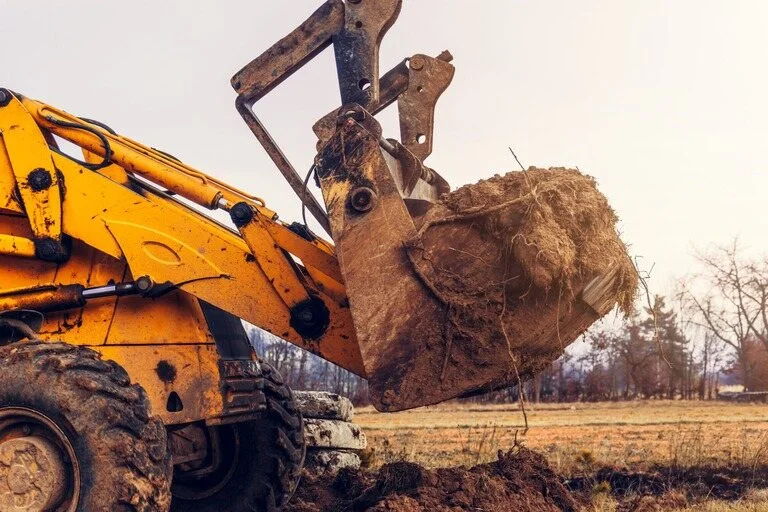 Closeup of large excavator with rubble in bucket mouth with trees in the background