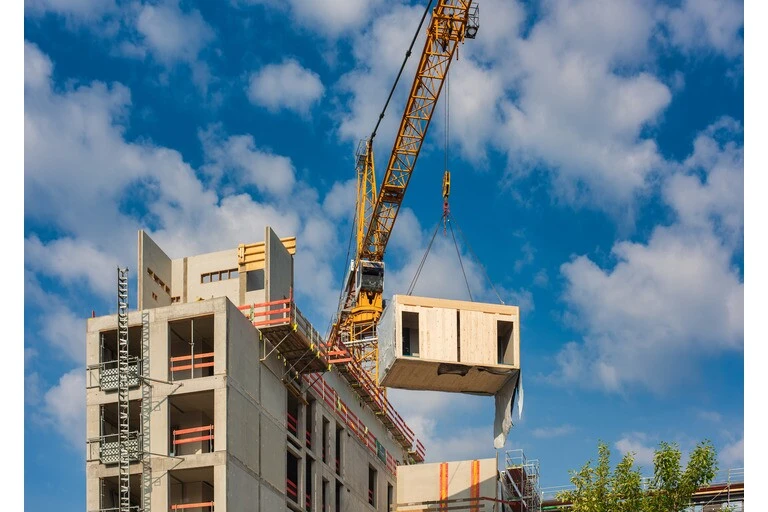 Crane lifting a wooden building module to its position in the structure. Construction site of an office building in Berlin. The new structure will be built in modular timber construction.