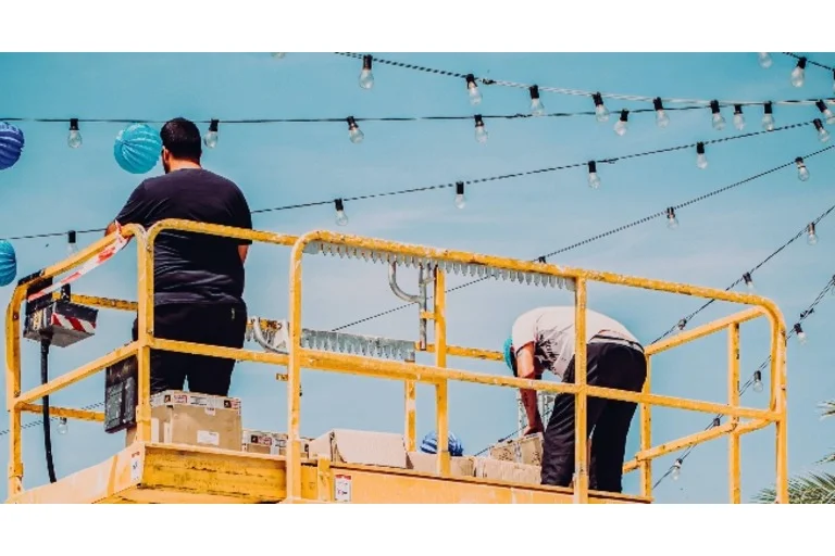 Workers on a cherrypicker putting up string lights