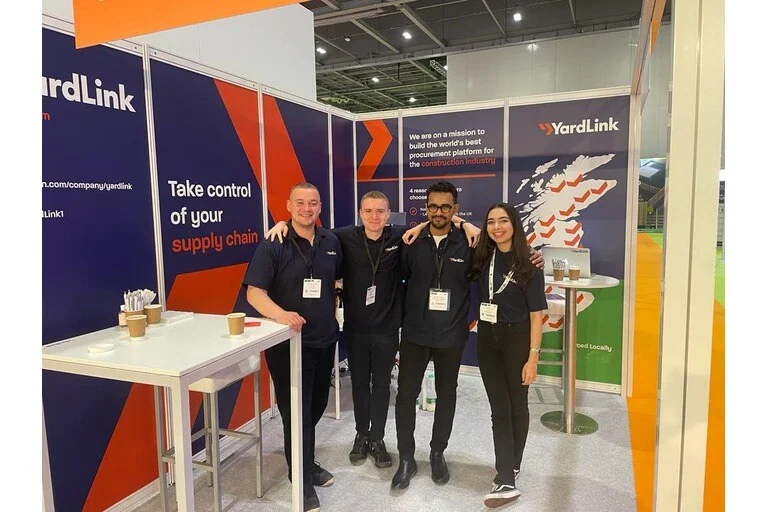 YardLink employees standing in front of exhibit at UK Construction Week at the ExCel, London.