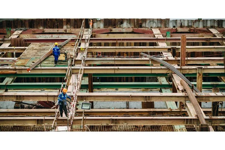 Employees working across beams at a construction site.